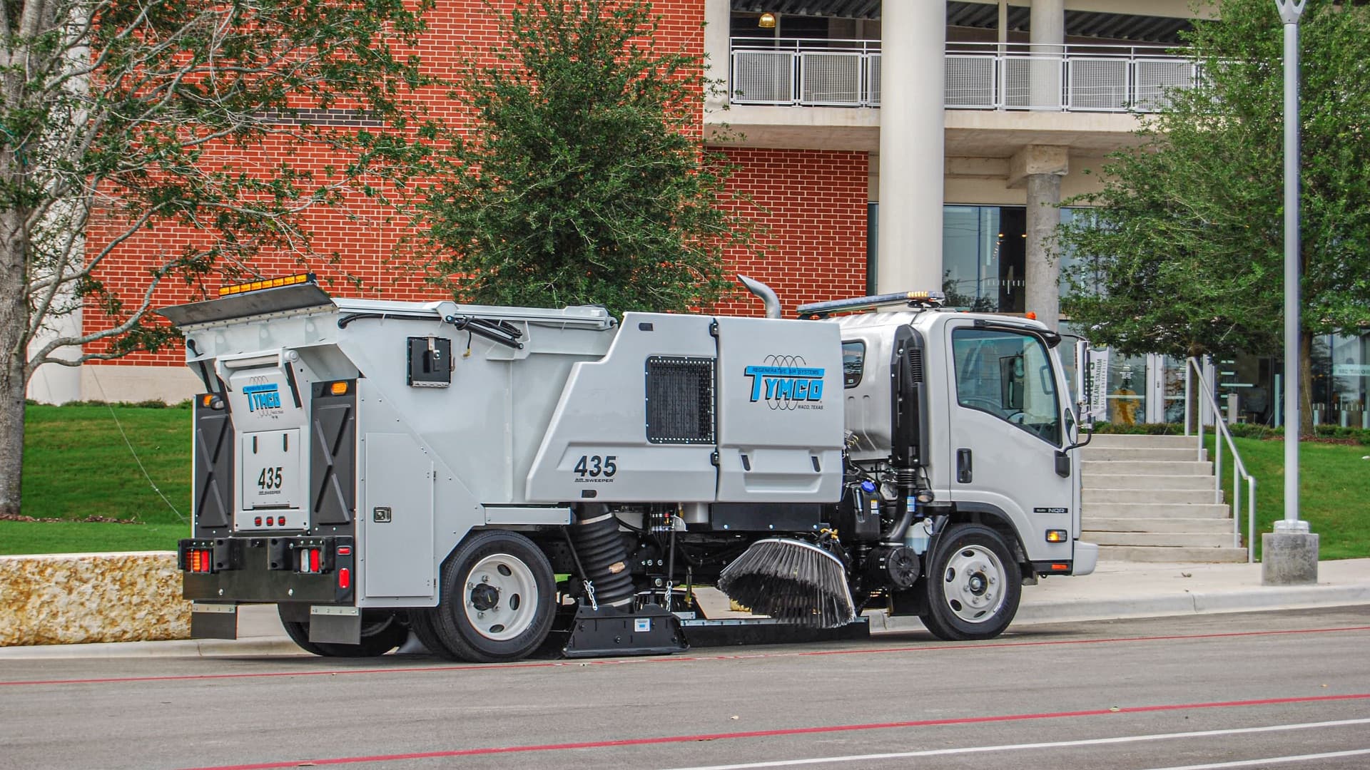 TYMCO Model 435 regenerative air sweeper cleaning a curb line along a city street